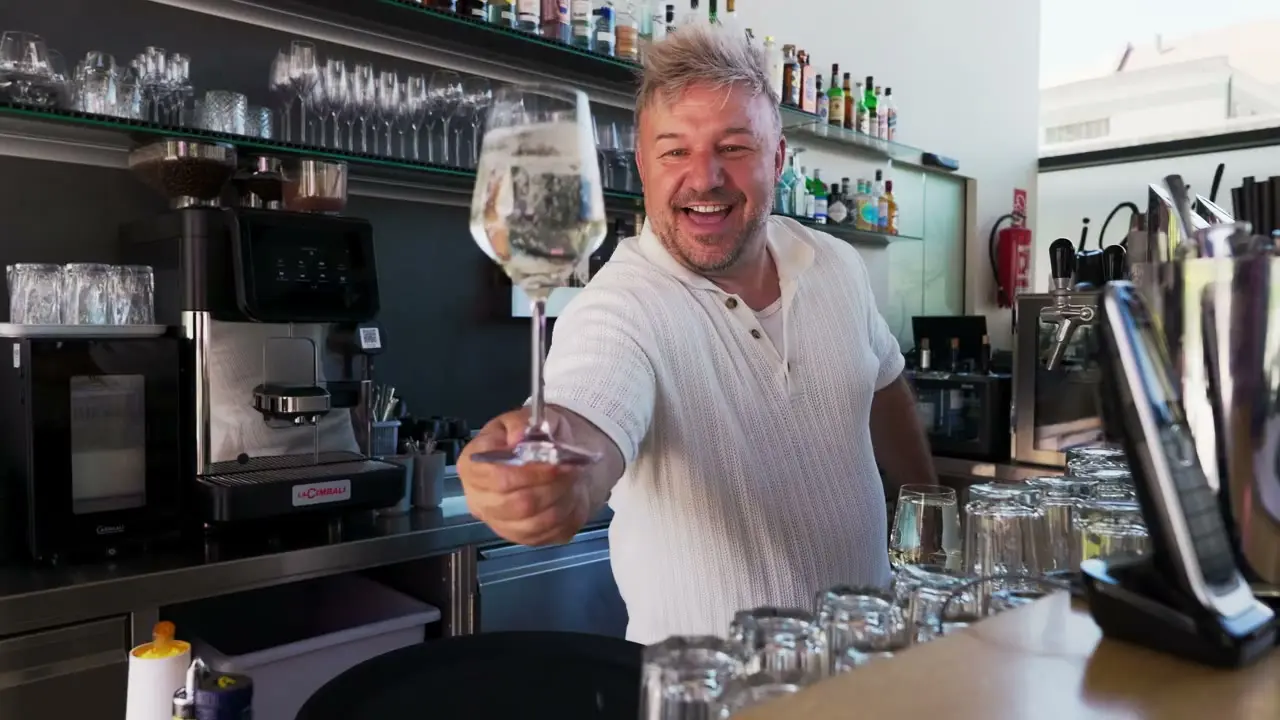 Barkeeper im Tapas Tapas reicht lachend ein Glas Wein über die Bar